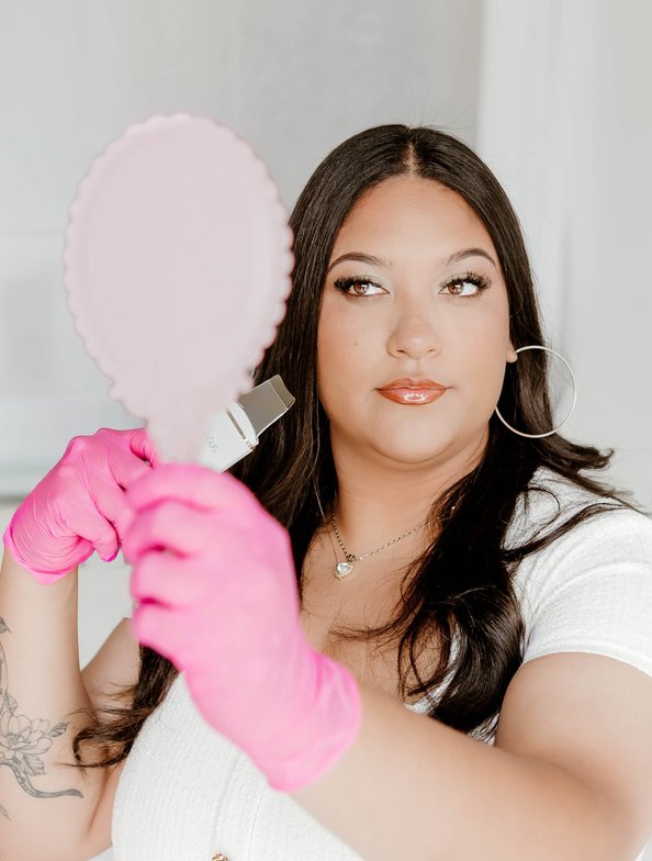 Monika Ortiz holding a hand mirror at Geespot Aesthetics in Colorado Springs